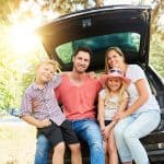 Happy family with children is sitting at the car in the summer