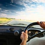 Driver’s hands on a steering wheel of a car and blue sky with cl